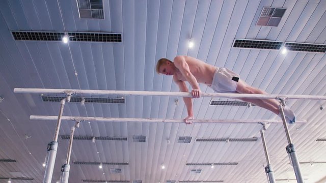 Gymnast performs routine on parallel bars HD gymnastics slow-motion video. Olympics athlete training skills and doing swings acrobatic exercises: hand support