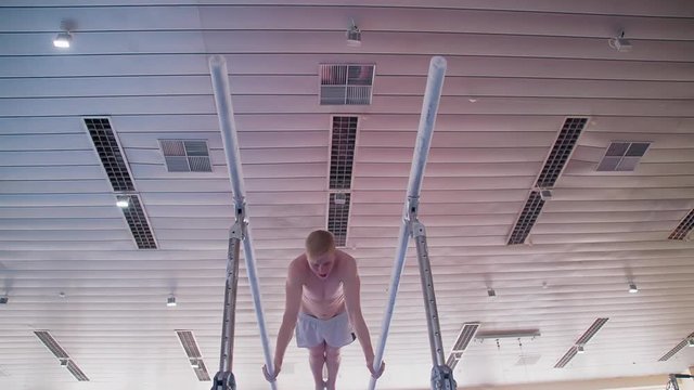 Gymnast performs routine on parallel bars HD gymnastics slow-motion video. Olympics athlete training skills and doing swings acrobatic exercises: hand support, somersault, flip