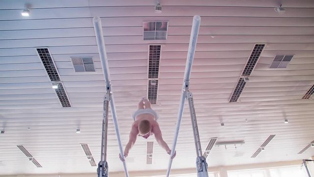 Gymnast performs routine on parallel bars HD gymnastics slow-motion video. Olympics athlete training skills and doing swings acrobatic exercises: hand support, somersault, flip
