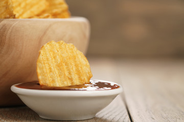 rippled potato chips with paprika and bbq sauce in wooden bowl, with copy space