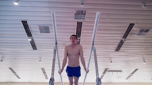 Gymnast performs routine on parallel bars HD gymnastics slow-motion video. Olympics athlete training skills and doing swings acrobatic exercises: hand support, somersault, flip