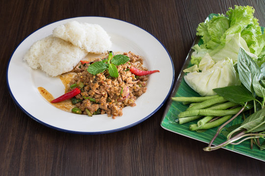 Ground pork salad with sticky rice and fresh vegetable Thai food and Thai called “Larb” on dark wooden table / Selective focus Image
