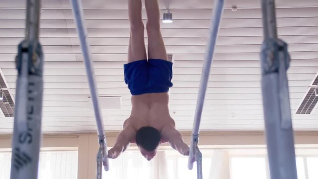 Gymnast performs routine on parallel bars HD gymnastics slow-motion video. Olympics athlete training skills and doing swings acrobatic exercises: handstand