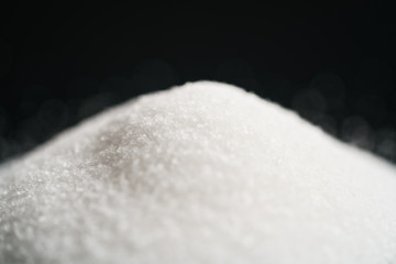white sugar heap on black background closeup photo, shallow focus