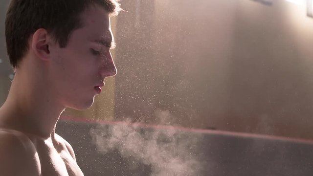 Athlete chalking hands wearing gymnastic grips before training HD slow-motion video. Close-up view of gymnast in sun light