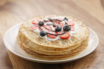 fresh blinis or crepes with fresh berries and cream decorated with chocolate sauce, sweet food