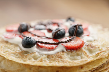 fresh blinis or crepes with fresh berries and cream decorated with chocolate sauce, closeup photo