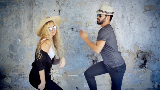 Happy young couple in sunglasses and hats dancing in slow motion listening to music having fun in love.