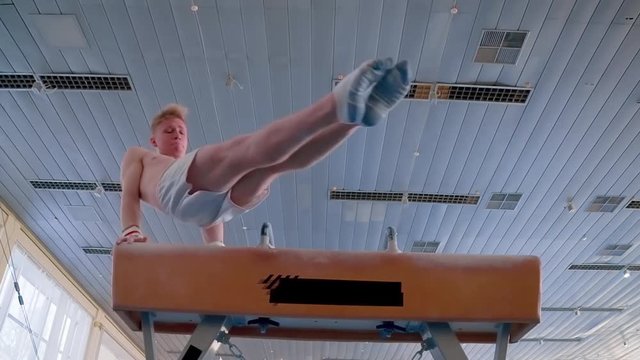Young gymnast doing routine exercises on pommel horse HD video. Olympics athlete training gymnastics skills: circles flairs trick performing, swings turning motion