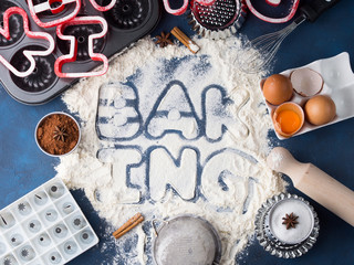 Flour letters spelling Baking with tools and sweet food ingredients sugar, eggs, cocoa, cinnamon. Top view flat lay concept