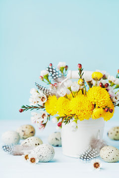 Easter greeting card with colorful flowers, feather and quail eggs on blue background. Beautiful spring composition.