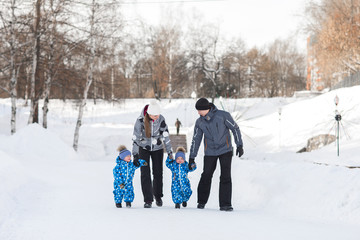 Fototapeta na wymiar Father, mother and children, twins hold each other hands and walking on the snow