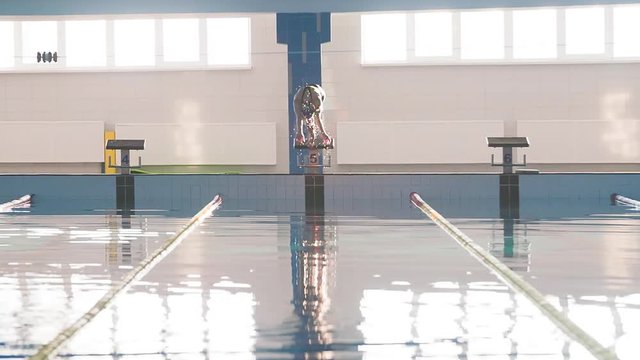 Female swimmer jumps off starting block and start swims in pool HD slow-motion video. Athlete training: dive and splash water surface