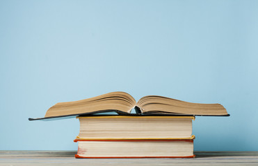 Open book, hardback books on wooden table and blue wall .Education background. Back to school. Copy space for text.