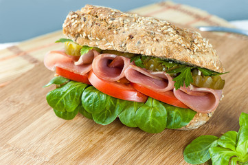 sandwich with ham, pickles, pepper, lettuce and tomato on the Board and napkin