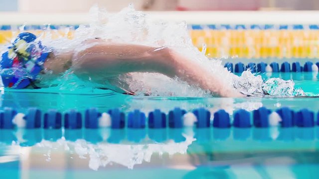 Female swimmer swims in pool HD slow-motion video. Butterfly professional athlete training. Come up from water, splashing, arms stroke. Side view