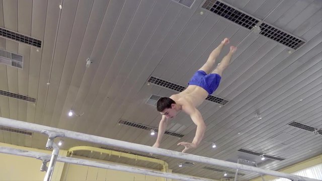 Gymnast performs routine on parallel bars HD gymnastics video. Olympics athlete training skills and doing swings acrobatic exercises: handstand, somersault, flip