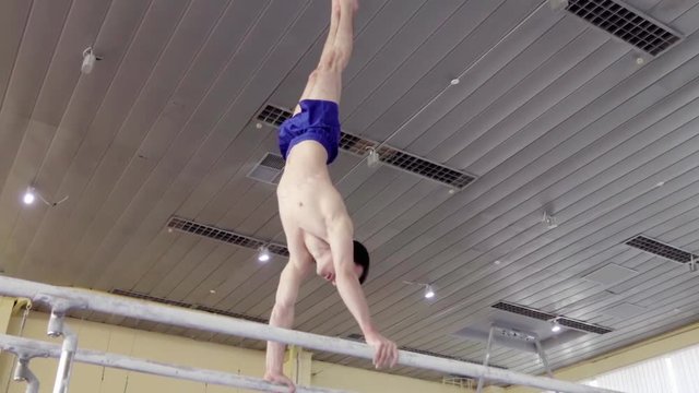 Gymnast performs routine on parallel bars HD gymnastics video. Olympics athlete training skills and doing swings acrobatic exercises: handstand, somersault, flip