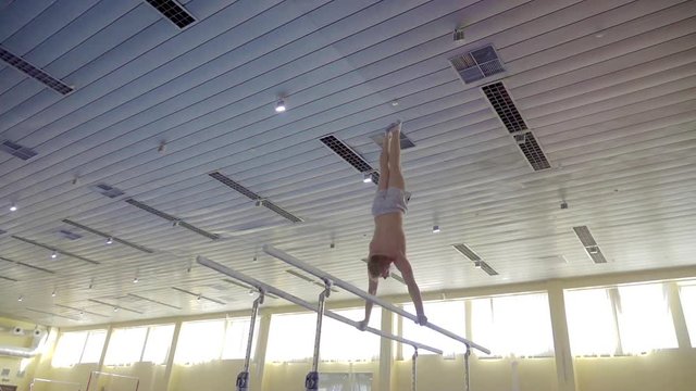 Gymnast performs routine on parallel bars HD gymnastics video. Olympics athlete training skills and doing swings acrobatic exercises: hand support, somersault, flip