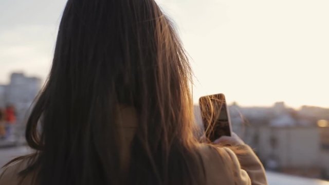 Unidentified woman take picture on her smartphone at city sunset