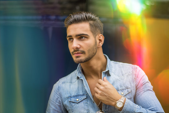 Attractive young man standing against colorful wall, looking to a side, wearing denim shirt