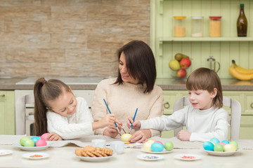 Obraz na płótnie Canvas Happy mother and child paint Easter eggs on the kitchen table