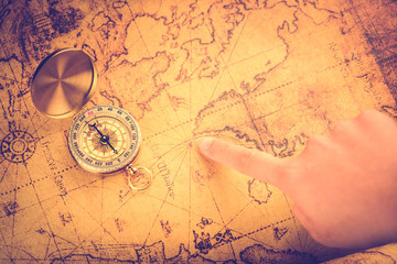 Close up of the hand holding a vintage compass over a vintage map