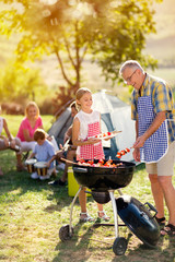 smiling grandfather and granddaughter grilling barbecue . - obrazy, fototapety, plakaty