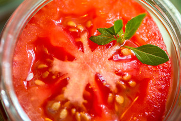 Canning fresh tomatoes with onions for winter in jelly marinade. A shot of basil leaves on top of a red ripe tomato slices and onion rings being put in jar.

