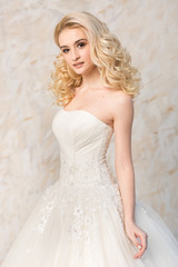 Fototapeta na wymiar a gorgeous smiling blonde bride with beautiful curly hair in a white wedding dress on a light background. beautiful young model with bridal hairstyle and makeup in a white magnificent dress.