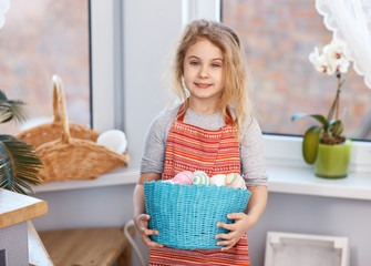 Little blonde girl holding basket with painted eggs. Easter day.