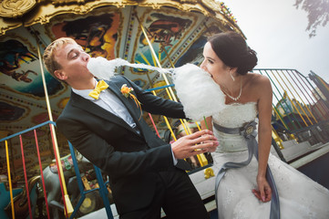 Wedding day. Happy couple. Bride and groom in amusement park eating cotton candy