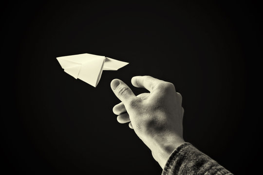 black and white image of a hand is throwing paper plane on black background.