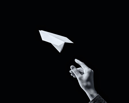 black and white image of a hand is throwing paper plane on black background.