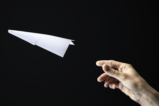 Image of a hand is throwing  white paper plane on black background.