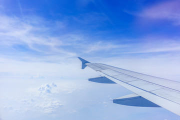 Looking thru airplane 's window seeing wing of airplane ,white clouds and blue sky