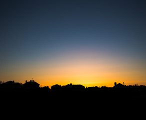 Evening sun setting behind a row of suburban houses