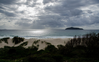 Sun breaking through storm clouds over remote beach and sand dunes