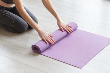 Young yoga Woman rolling her lilac mat - obrazy, fototapety, plakaty