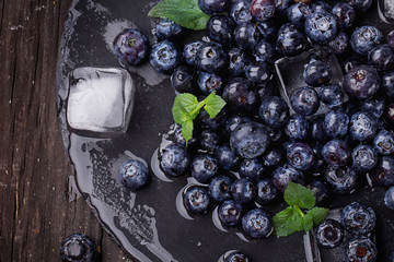 Blueberries on a stone slate board wth ice cubes and mint leaves over a rustic wooden board