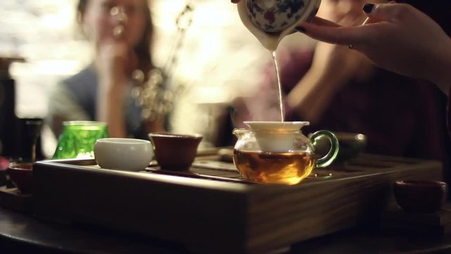 Tea ceremony in the cafe, the waiter pours the tea, the people sitting at the table
