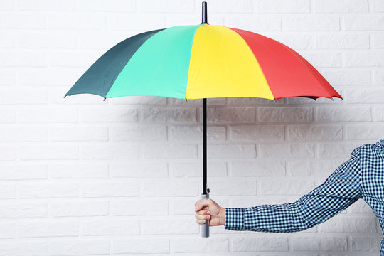 Colorful umbrella in male hand on brick wall background