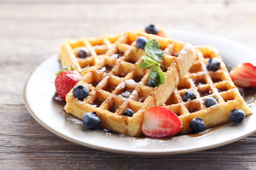Homemade waffles with berries in plate on grey wooden table