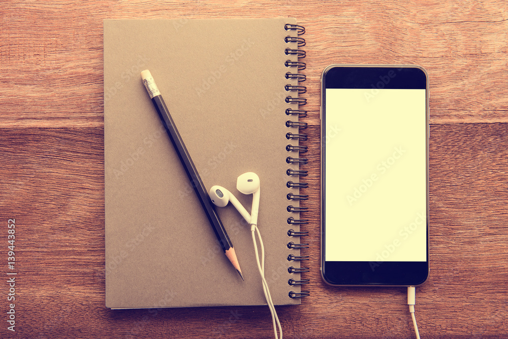 Aufkleber Smartphone with white screen and Note book On Wooden Table With Copyspace