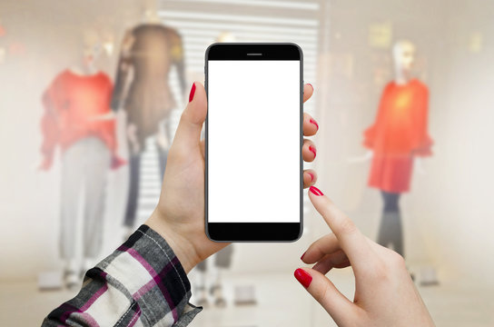Women in boutique holding smartphone in hands with blank display, shopping online concept. Maneken dolls in boutique window in background