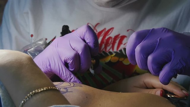 Tattoo master in gloves makes the tattoo on a woman's body close-up