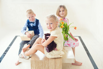 Beautiful funny toddler girl sitting in room laugh. Guests children give her a present and bouquet of tulips