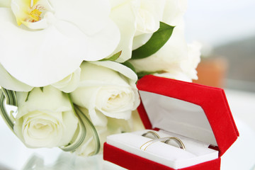 beautiful wedding bouquet of roses and orchids and red velvet box with gold and platinum wedding rings on glass table