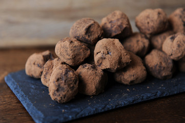 Chocolate truffles in cocoa sprinkled. On the slate board on wooden background. Close-up, texture