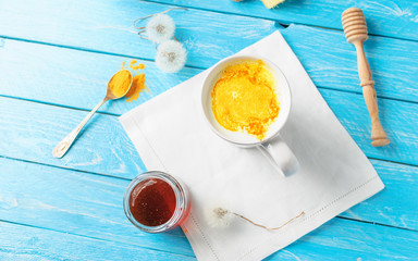 Ayurvedic golden milk with turmeric powder, honey and ginger in blue wooden background. flu remedy,...